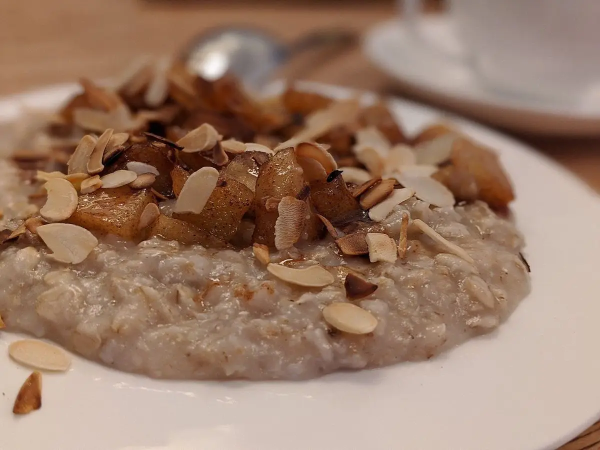 Porridge de avena cremoso cubierto de almendras laminadas y fruta caramelizada en un plato blanco