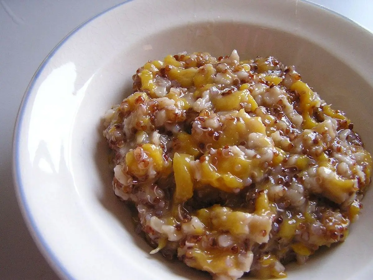 Plato blanco de gachas de quinoa con trozos de fruta amarilla caramelizada