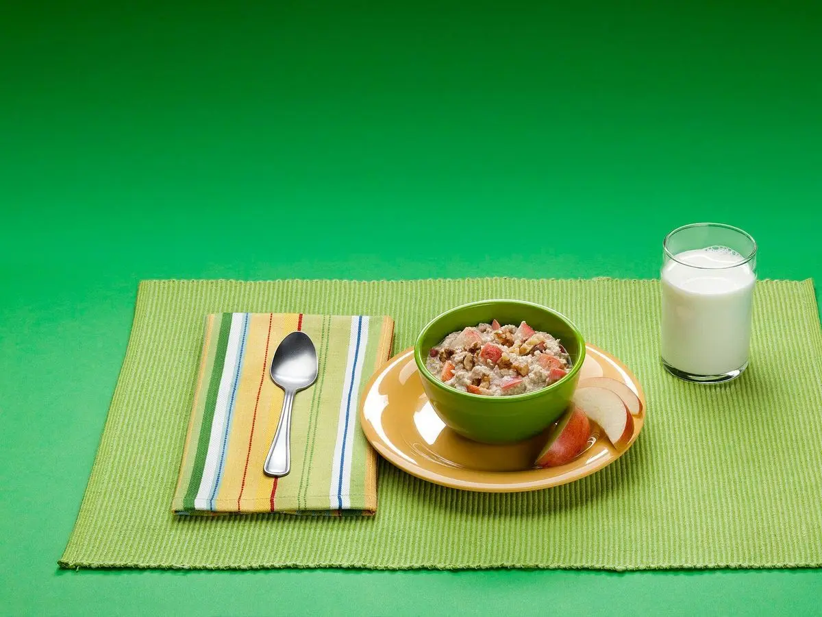 Cuenco verde de cereales integrales con un vaso de leche y una servilleta sobre fondo verde