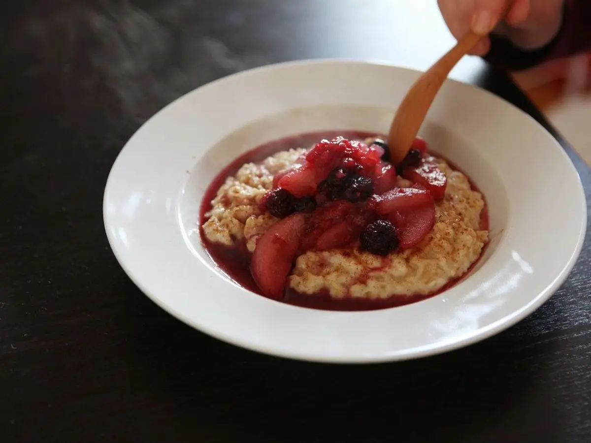Plato hondo blanco de avena cocida con frutos rojos y una cuchara