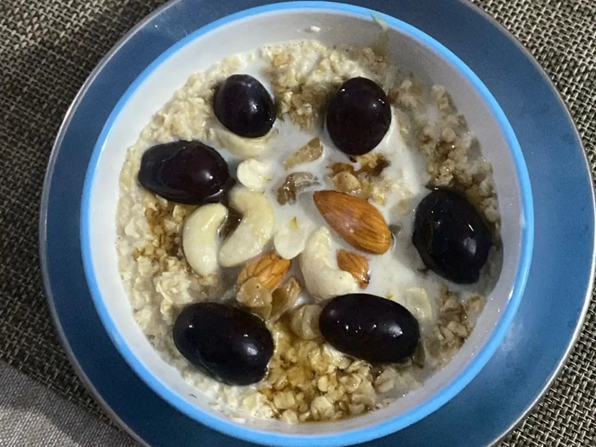 Bol de avena con leche cubierto de anacardos, almendras, pasas y uvas negras