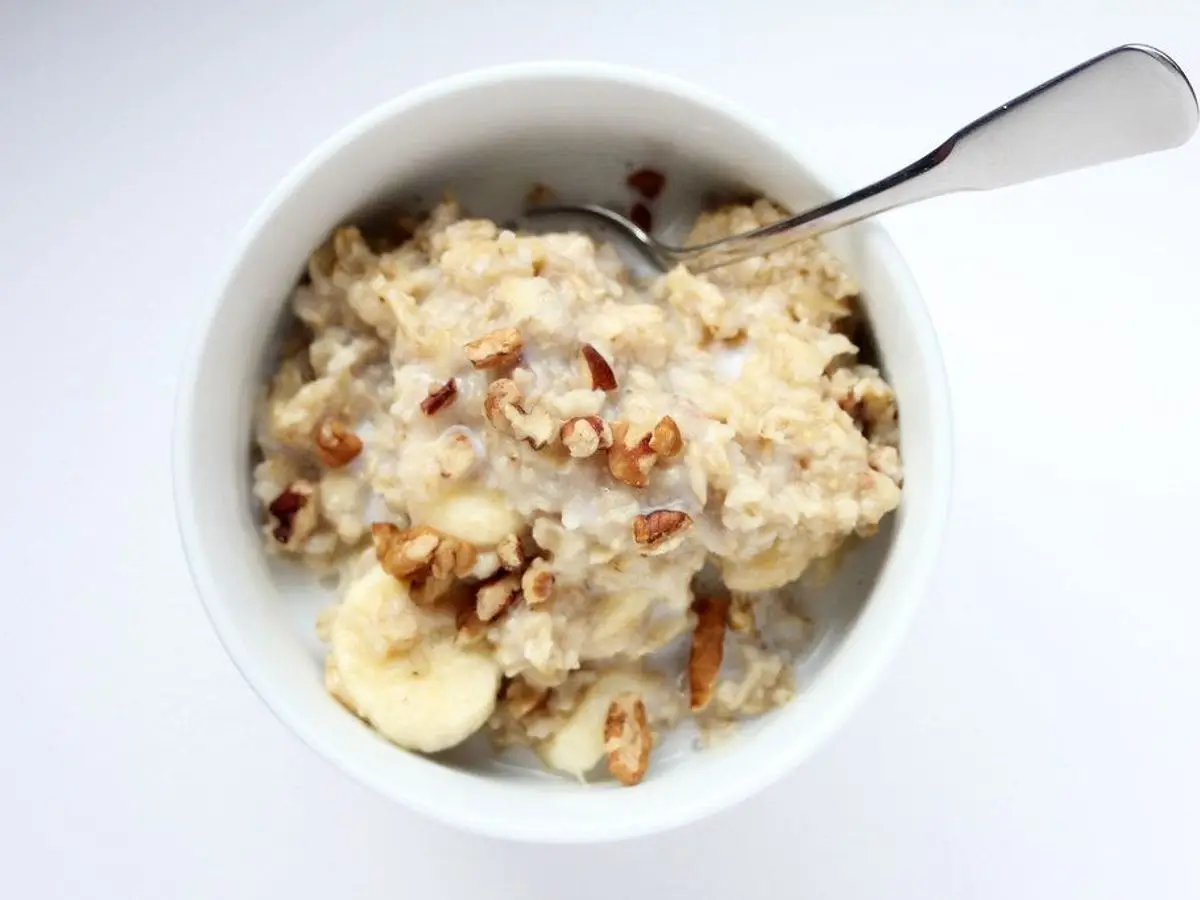 Cuenco blanco de avena cremosa con rodajas de plátano y nueces picadas y una cuchara