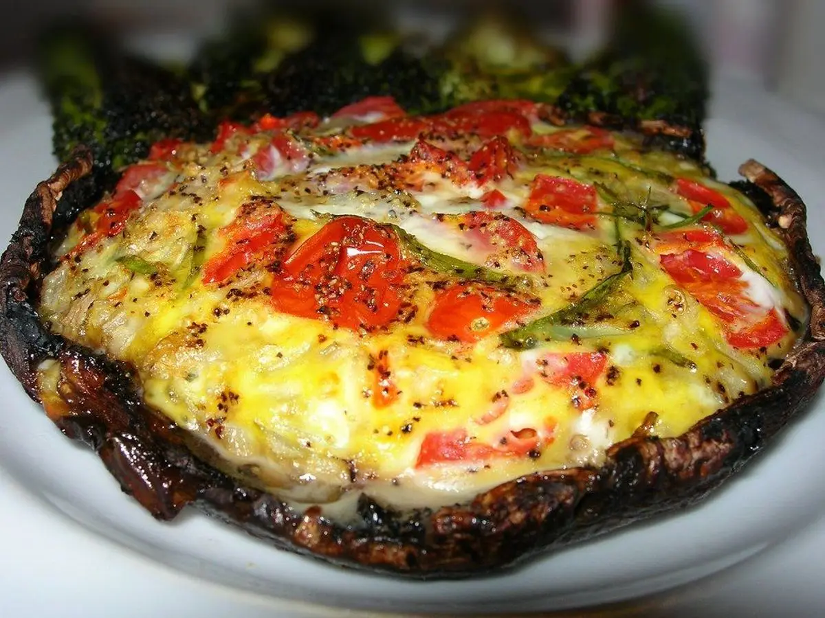 Champiñón portobello relleno de huevo cuajado con rodajas de tomate rojo por encima
