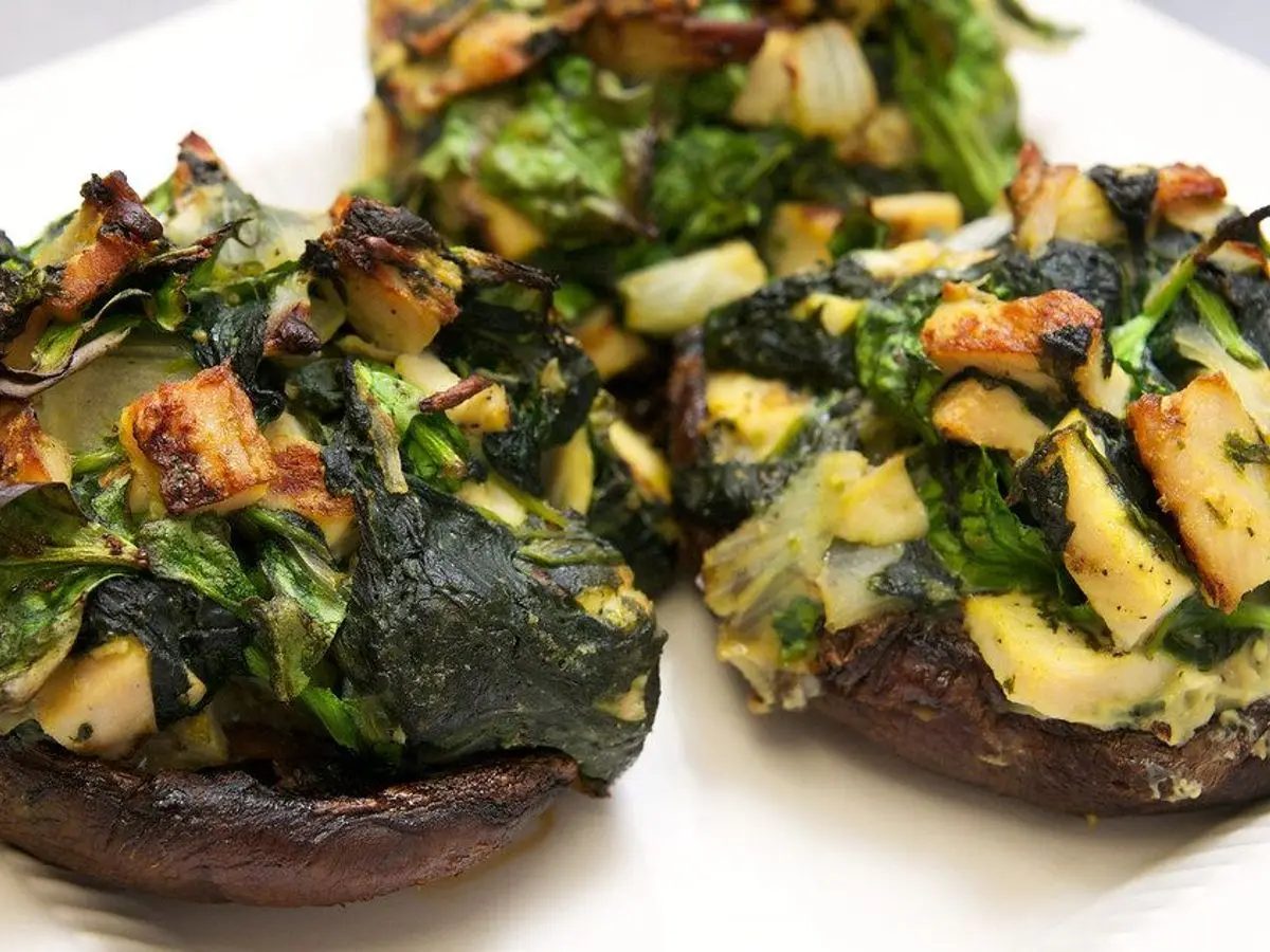 Champiñones portobello rellenos de espinacas y verduras salteadas sobre un plato blanco