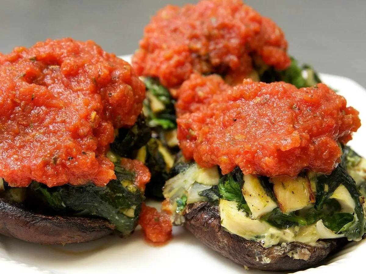 Champiñones portobello rellenos de espinacas con salsa de tomate por encima sobre un plato blanco