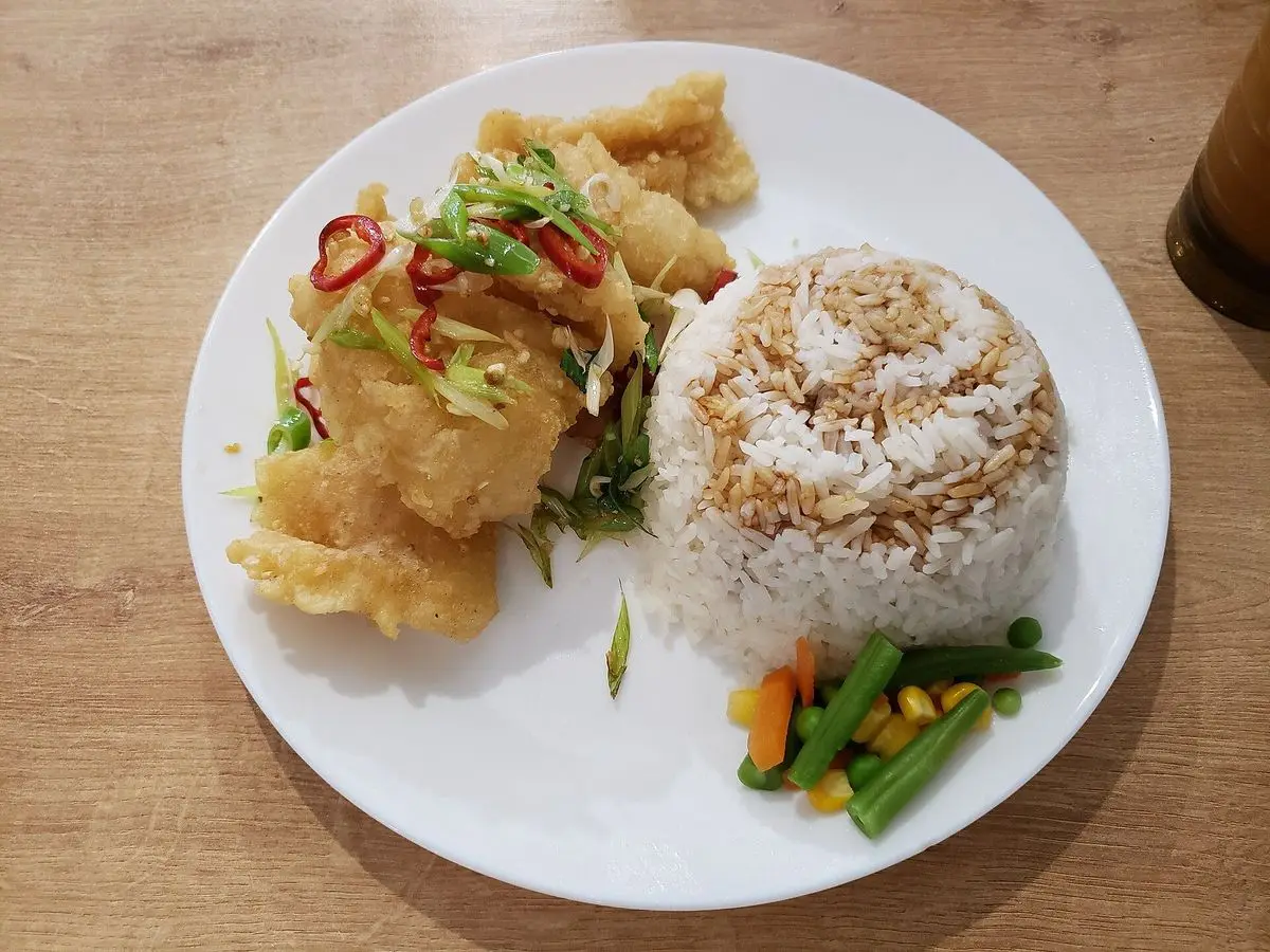 Plato blanco de calamar con pimiento y cebolleta junto a una porción de arroz blanco y guisantes con zanahoria