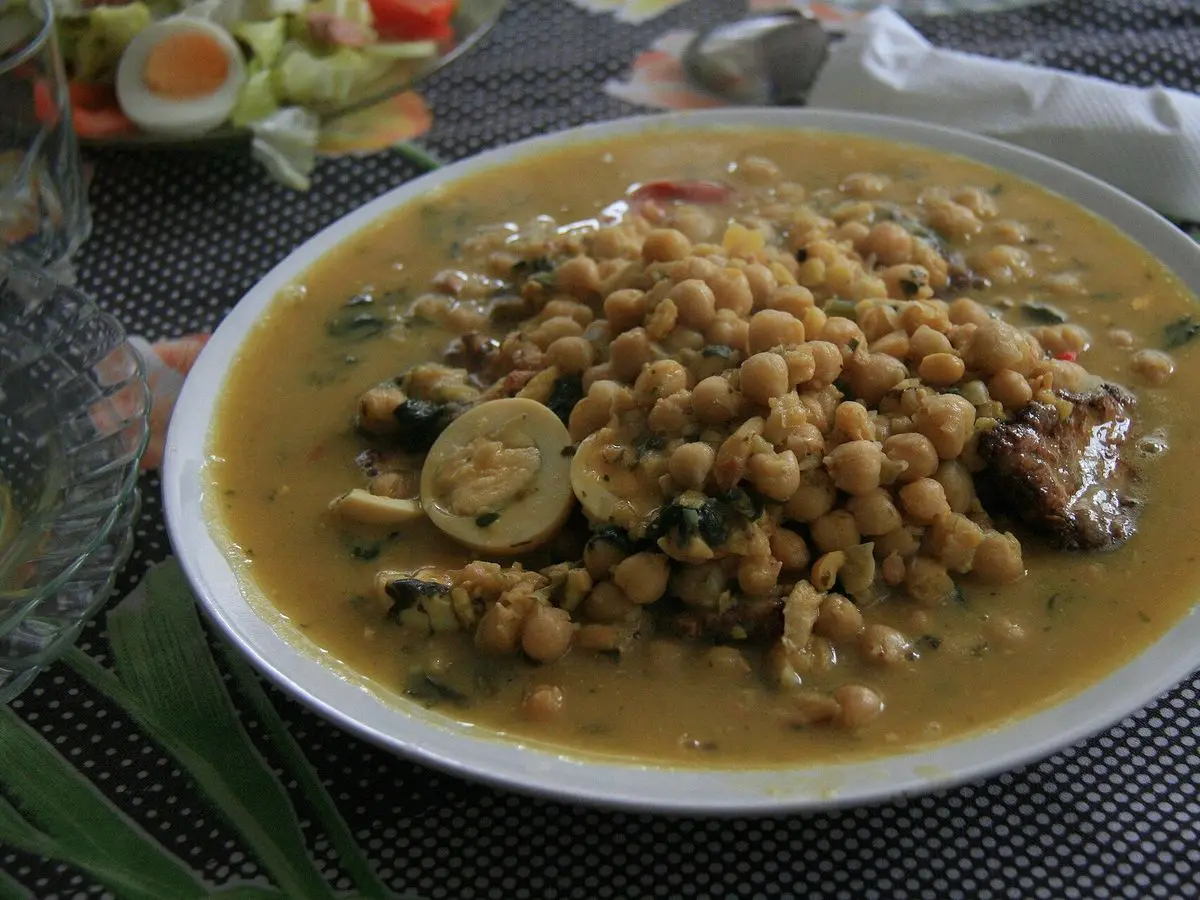 Plato hondo de potaje de legumbres con caldo verdoso y medio huevo duro sobre un mantel oscuro