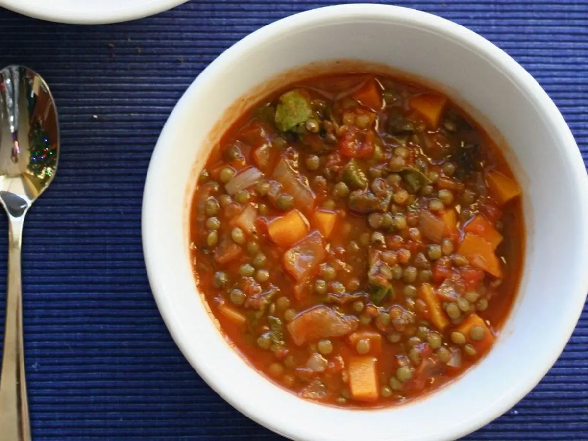 Cuenco blanco de guiso de lentejas con tomate, verduras en dados y cuchara