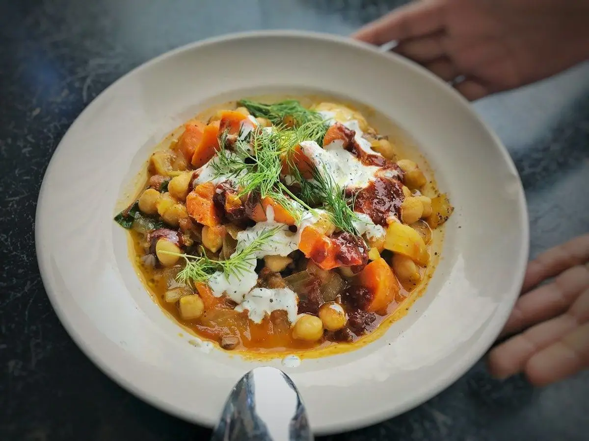 Plato hondo blanco con garbanzos guisados, zanahoria y hierbas frescas