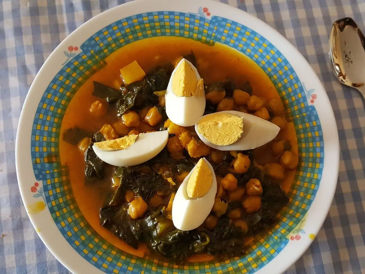 Plato de potaje de garbanzos con espinacas y huevo duro partido en cuartos sobre mantel de cuadros