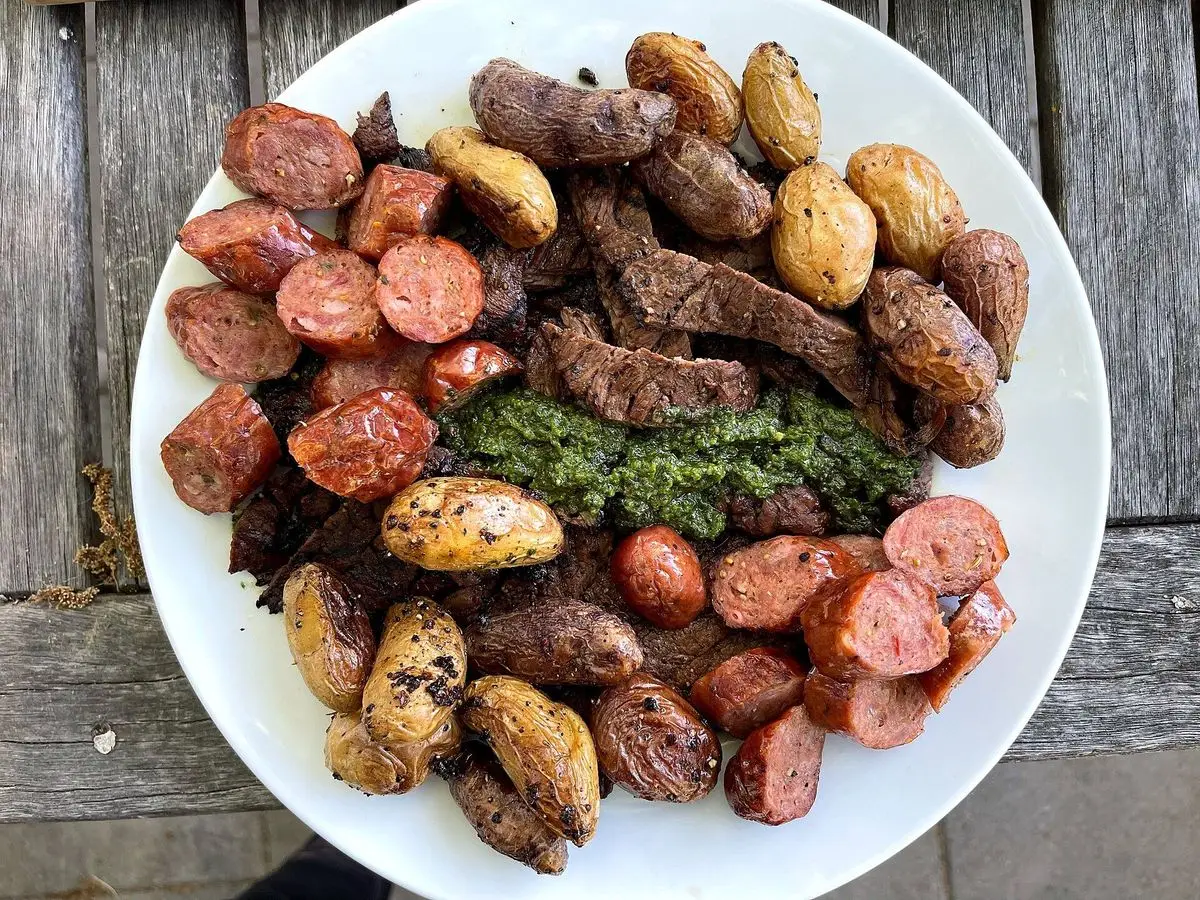 Plato de carne de cerdo a la brasa con patatas pequeñas, salchicha y salsa verde de hierbas