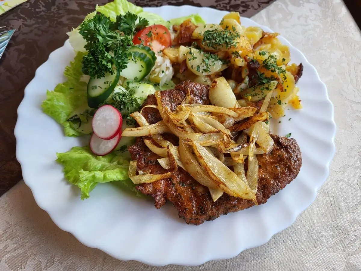 Plato blanco con filete de cerdo a la plancha, patatas salteadas con cebolla y ensalada de lechuga y rábano