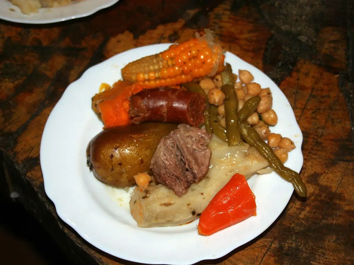 Plato blanco con puchero de mazorca de maíz, patata, carne, garbanzos y pimiento rojo