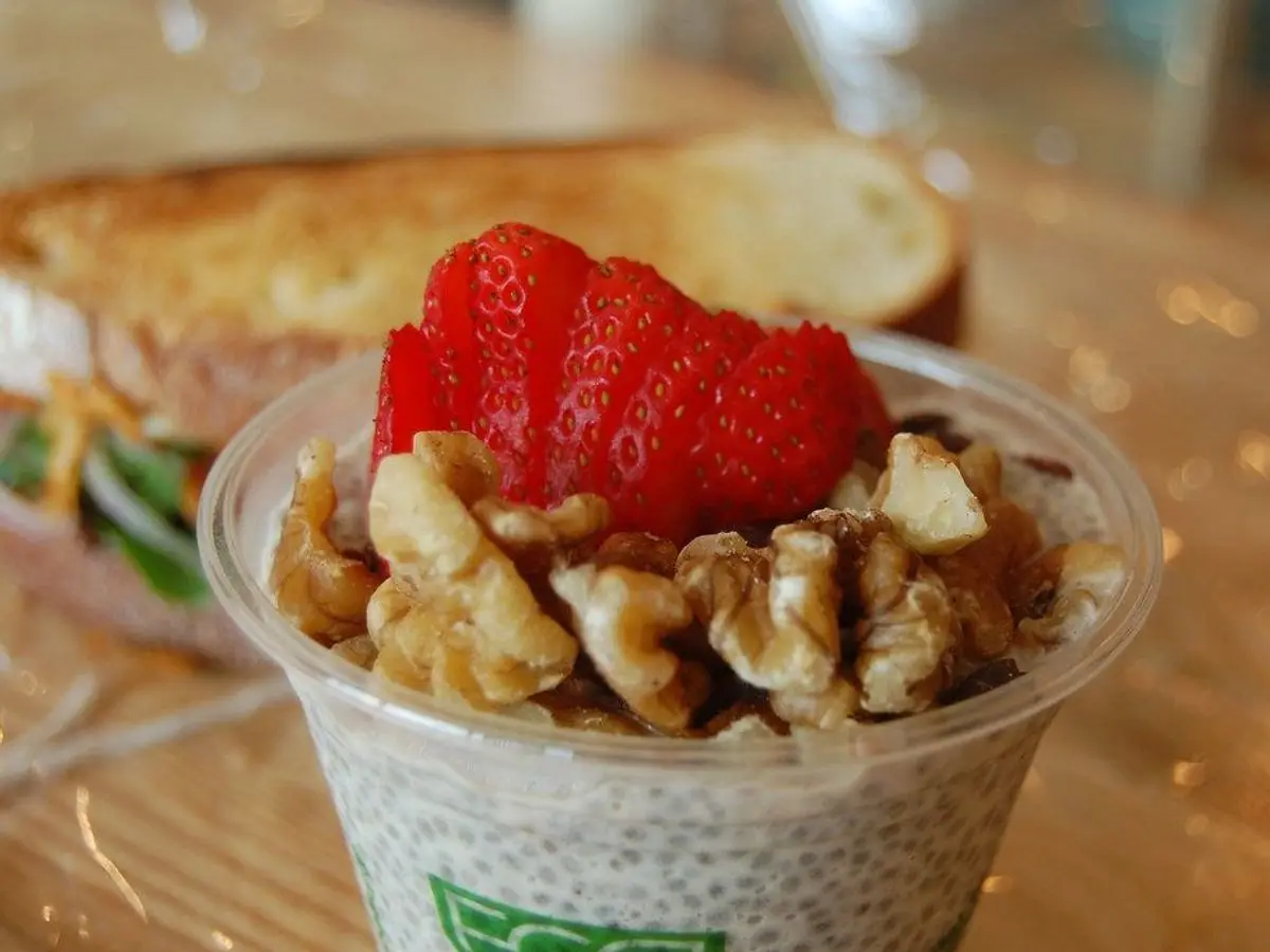 Vasito de pudin de chía con fresa y nueces troceadas por encima, junto a una tostada