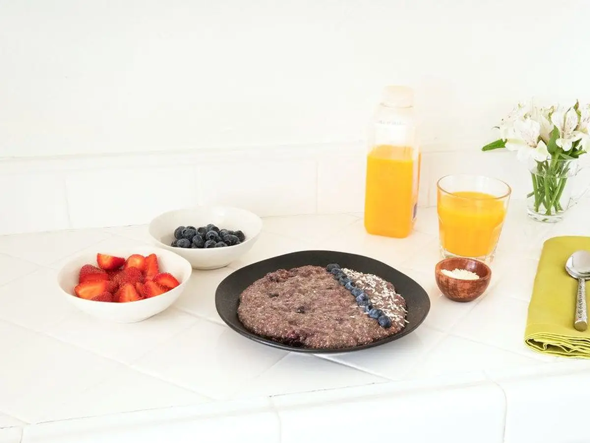 Plato negro con pudin de chía coronado de arándanos y coco rallado, con fresas, arándanos y zumo de naranja alrededor