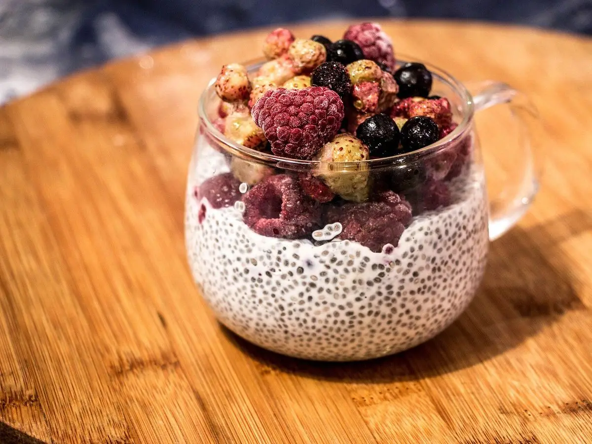 Taza de cristal con pudin de chía coronado de frambuesas y moras sobre una tabla de madera