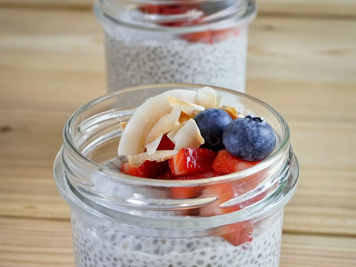 Tarro de pudin de chía con leche de coco, láminas de coco, arándanos y fresas por encima