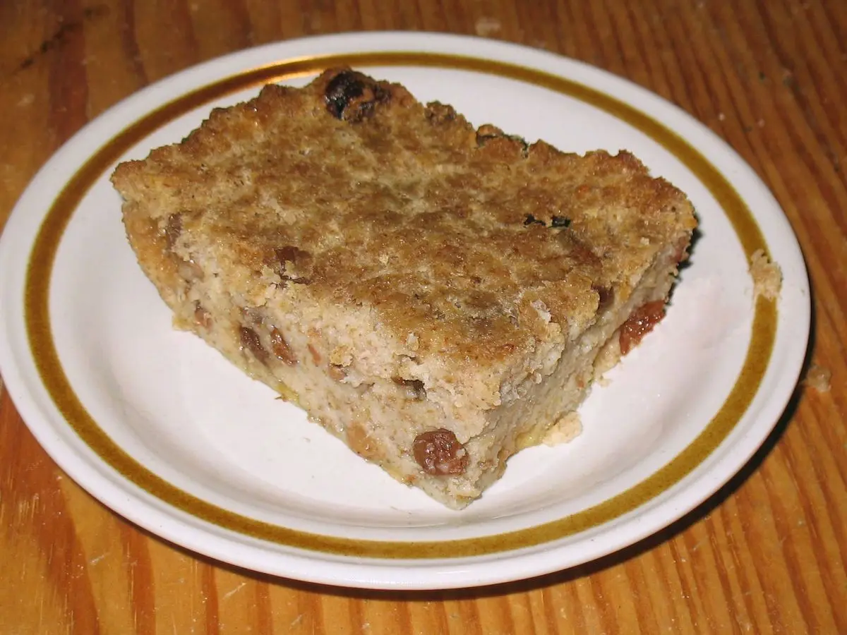 Porción de pudin de pan horneado con pasas sobre un plato blanco con filo dorado