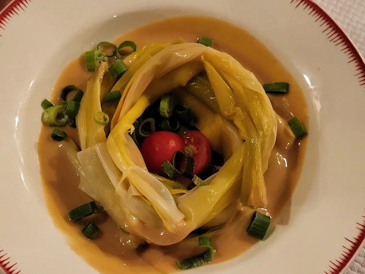 Plato con puerros cocidos enrollados en vinagreta, con cebollino picado y dados de tomate