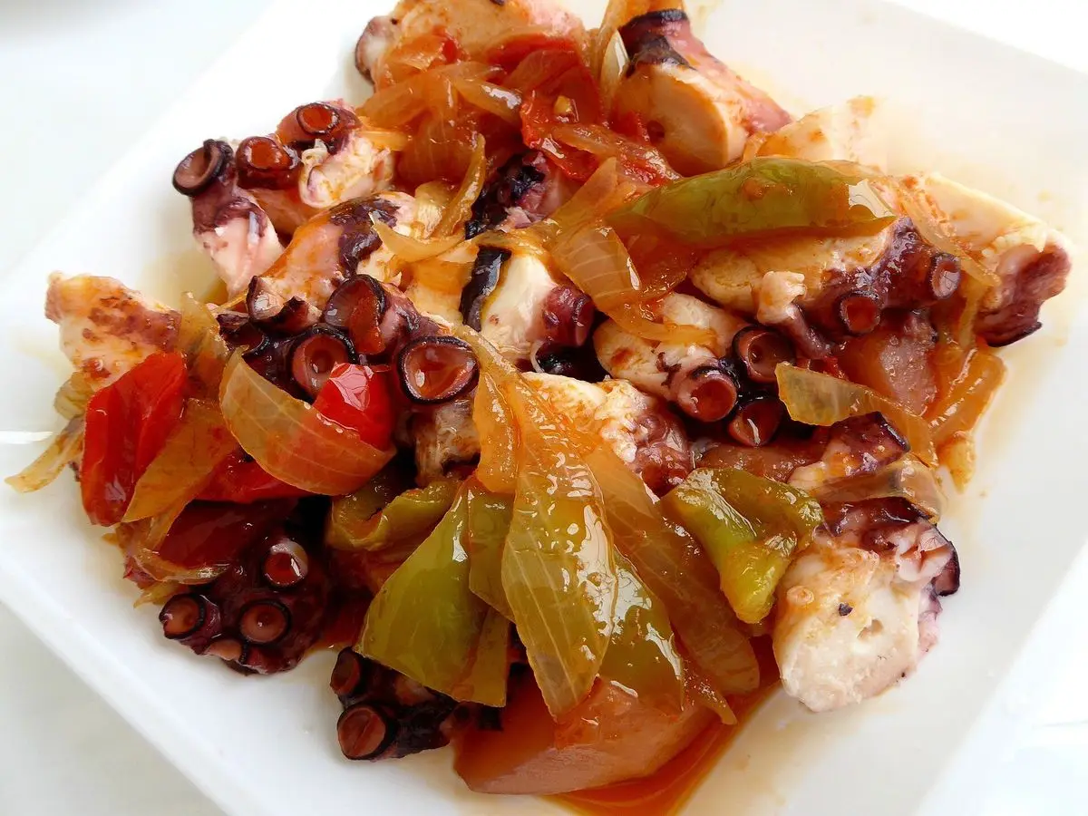 Plato blanco de pulpo troceado guisado con cebolla y pimientos verdes y rojos