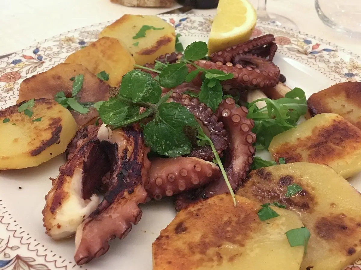 Pulpo asado con patatas doradas, perejil fresco y medio limón en un plato