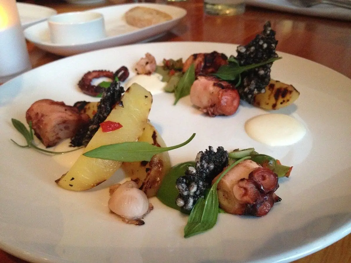 Plato blanco con pulpo asado, patata, hierbas y aceitunas negras
