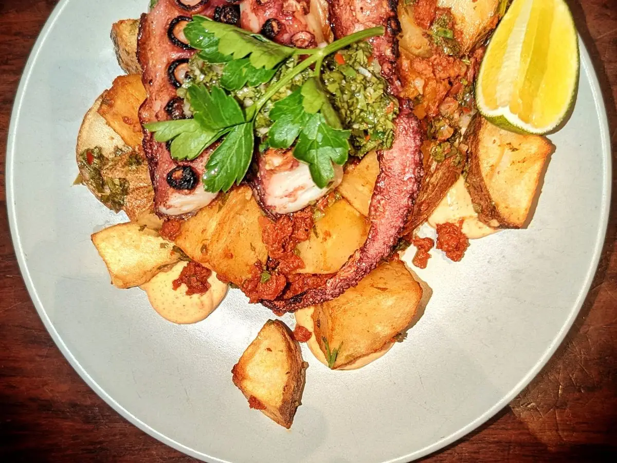 Plato de pulpo a la plancha con patatas doradas, salsa verde y gajo de limón