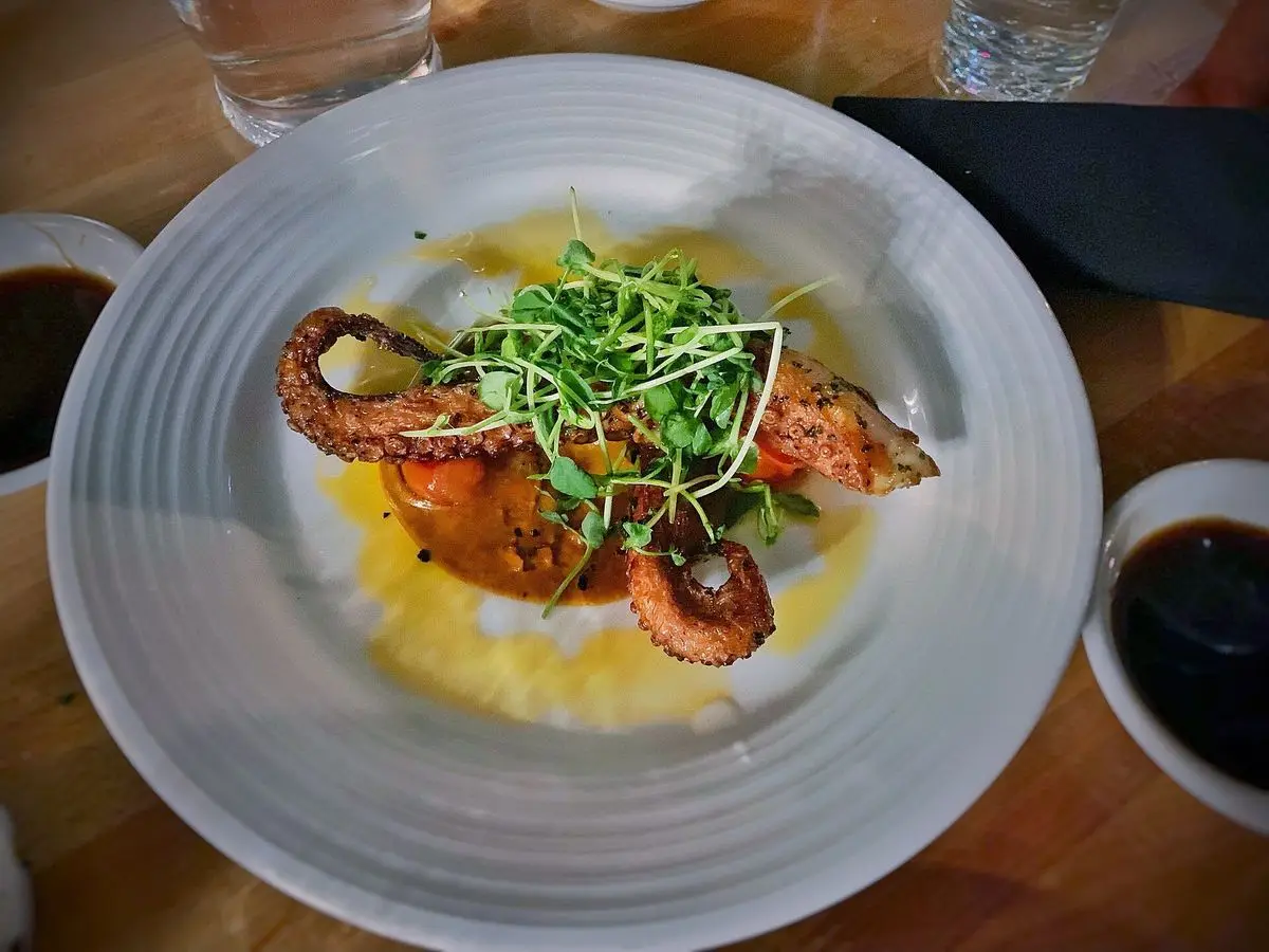 Pulpo a la parrilla sobre una crema amarilla con brotes verdes en un plato blanco
