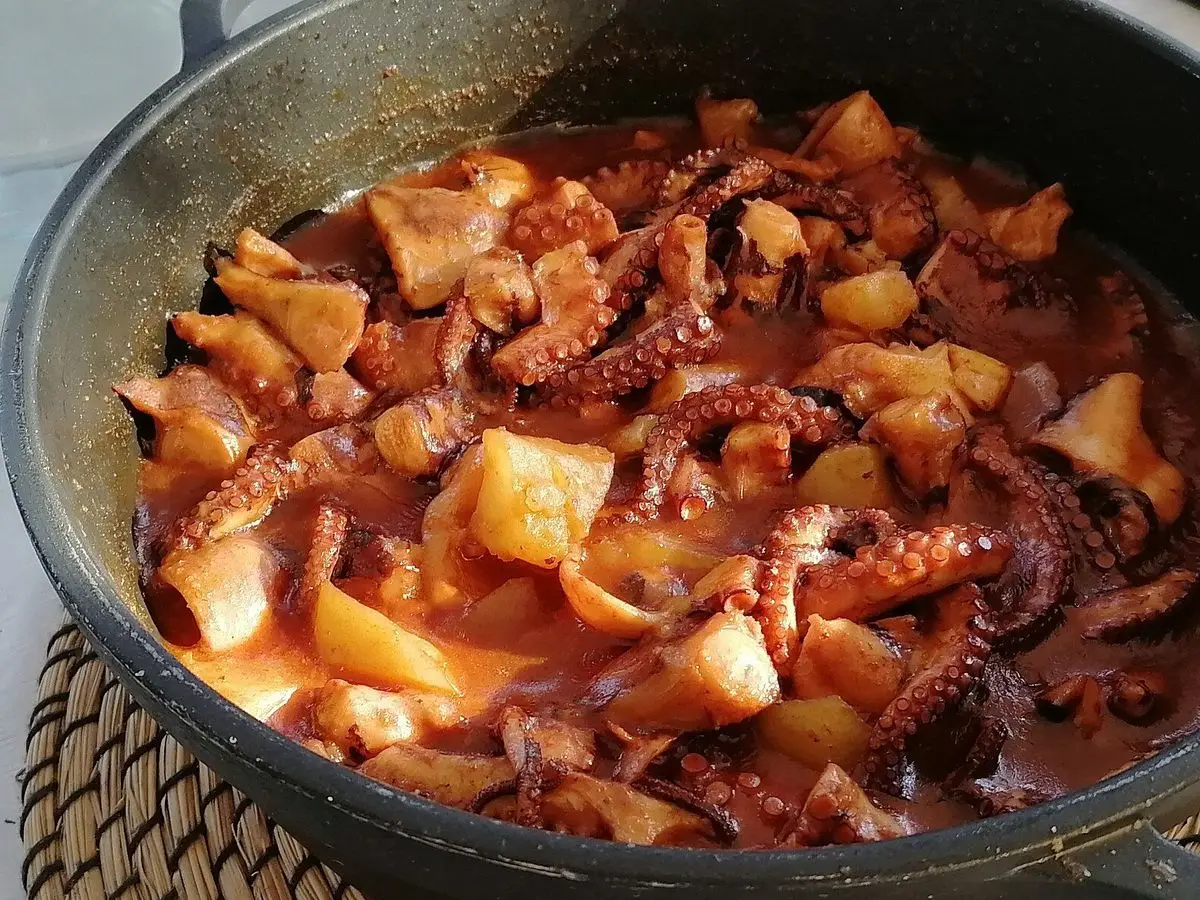 Cazuela de pulpo guisado en salsa de tomate con patata en una olla oscura