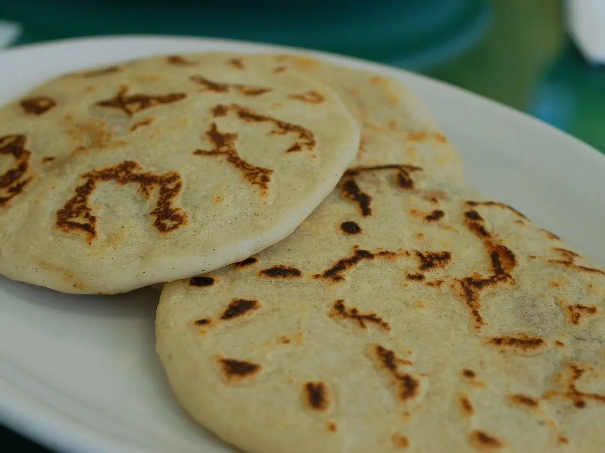 Plato blanco con dos pupusas de maíz doradas a la plancha