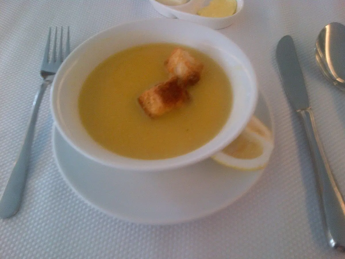 Cuenco blanco de crema de lentejas con picatostes sobre un mantel claro con cubiertos