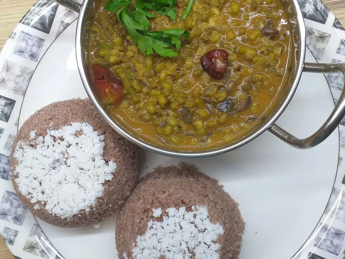 Puttu de arroz con coco rallado servido junto a un cuenco con guiso especiado de legumbres y cilantro