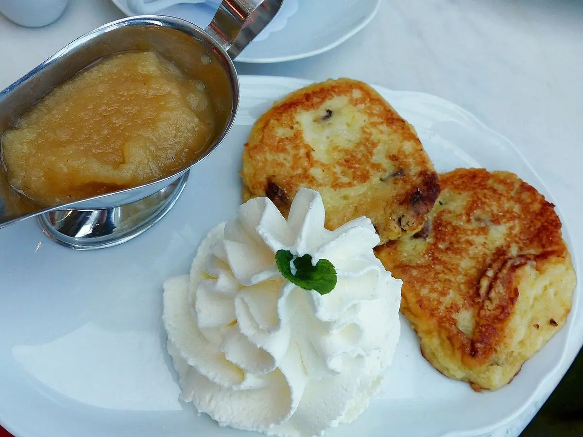 Dos tortitas doradas de patata y quark con nata montada y una salsera de compota de manzana