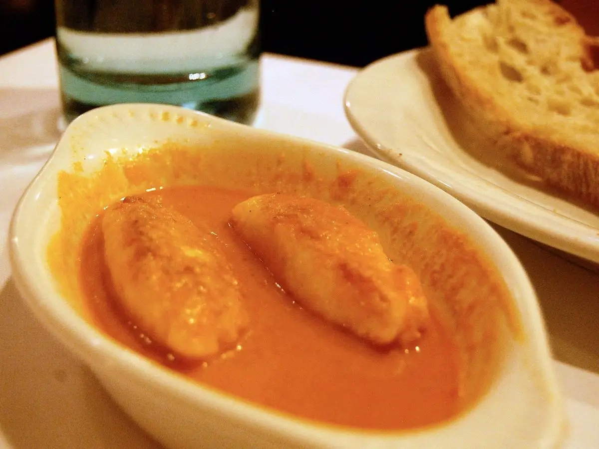 Quenelles de pescado gratinadas en salsa anaranjada en una fuente blanca con pan al lado