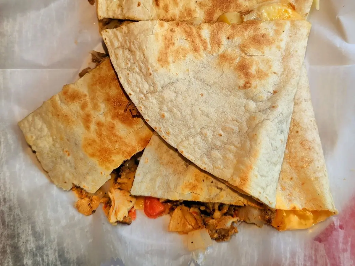 Quesadilla de tortilla dorada cortada en triángulos con relleno visible sobre papel