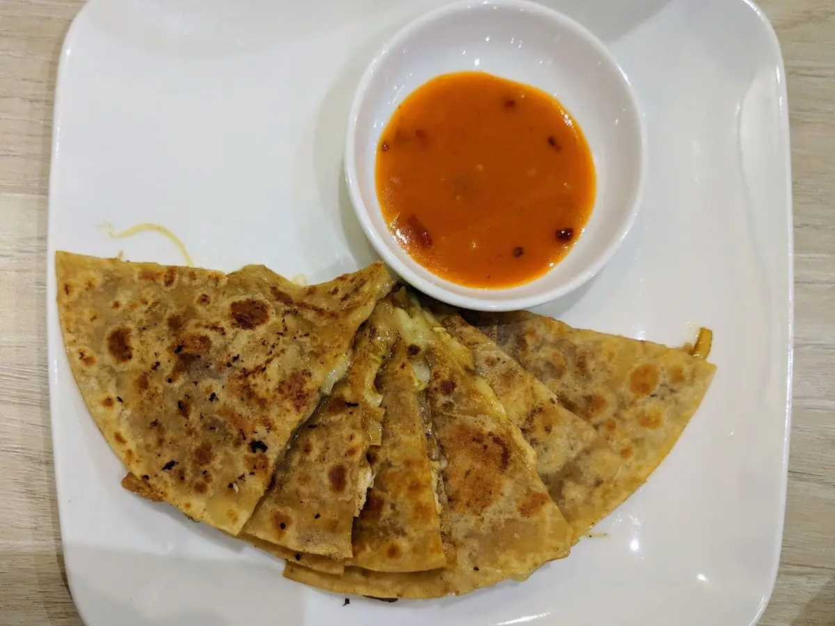 Tortilla rellena y tostada cortada en triángulos, con un cuenco de salsa de tomate en un plato blanco