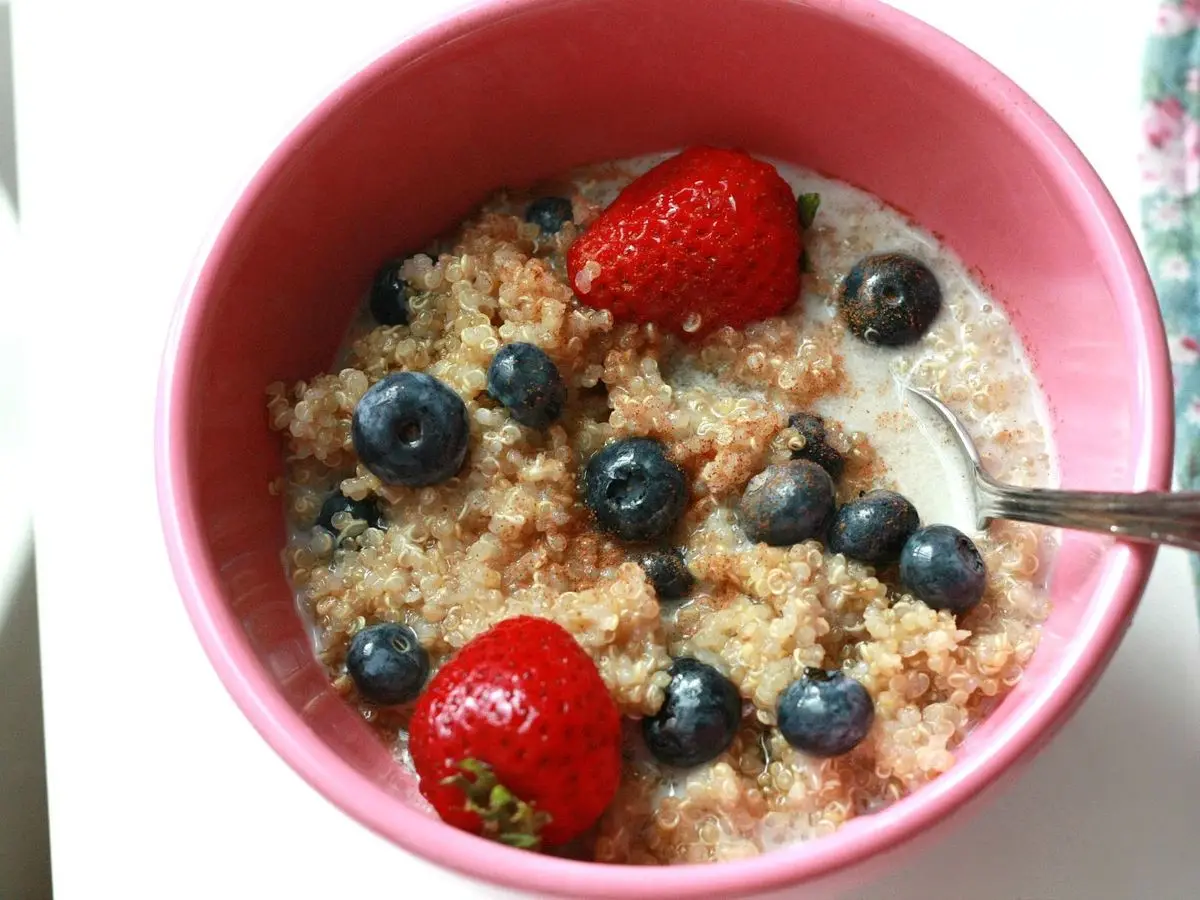Cuenco rosa de cereal cocido con leche, arándanos y fresas con una cuchara