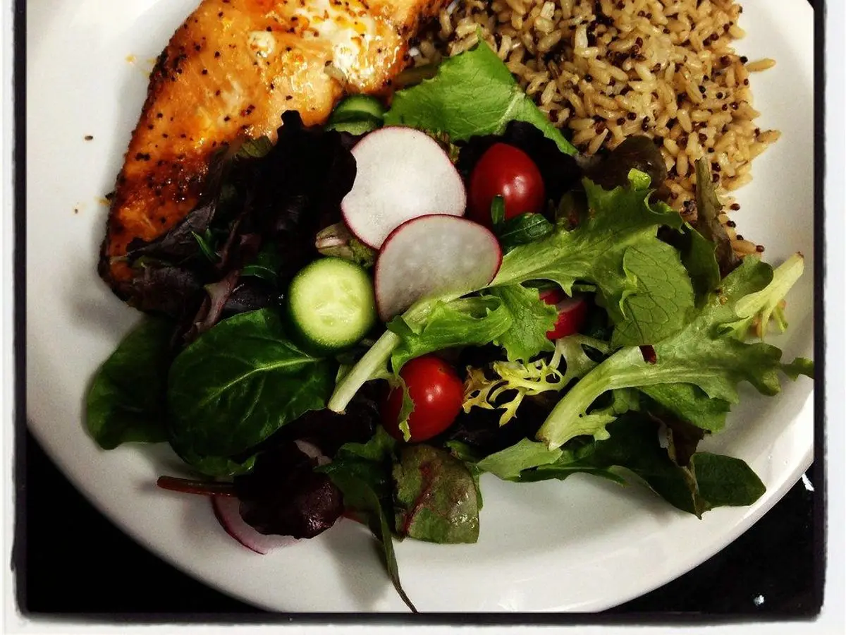 Plato con filete de pollo dorado, arroz integral y ensalada de hojas verdes, rábano y tomate