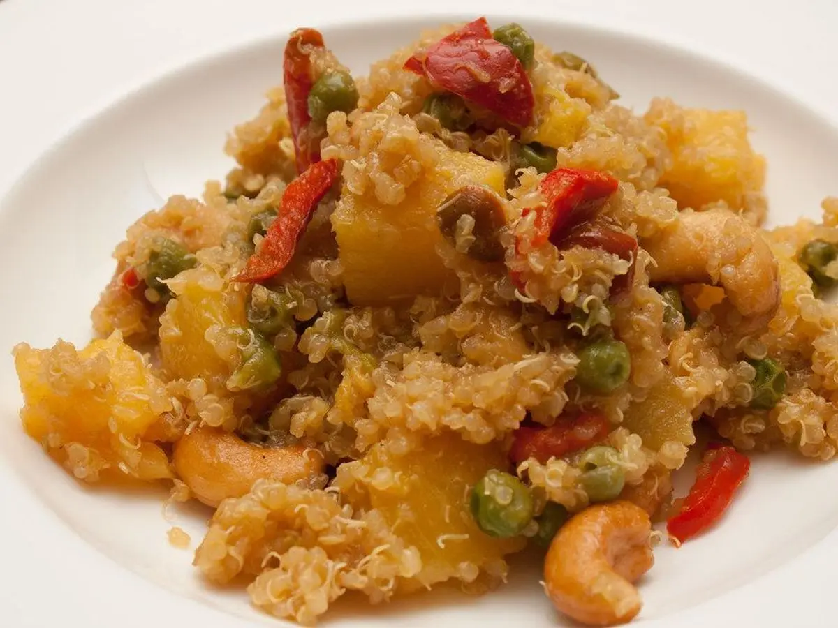 Plato blanco de quinoa salteada con guisantes, pimiento rojo, trozos de piña y anacardos