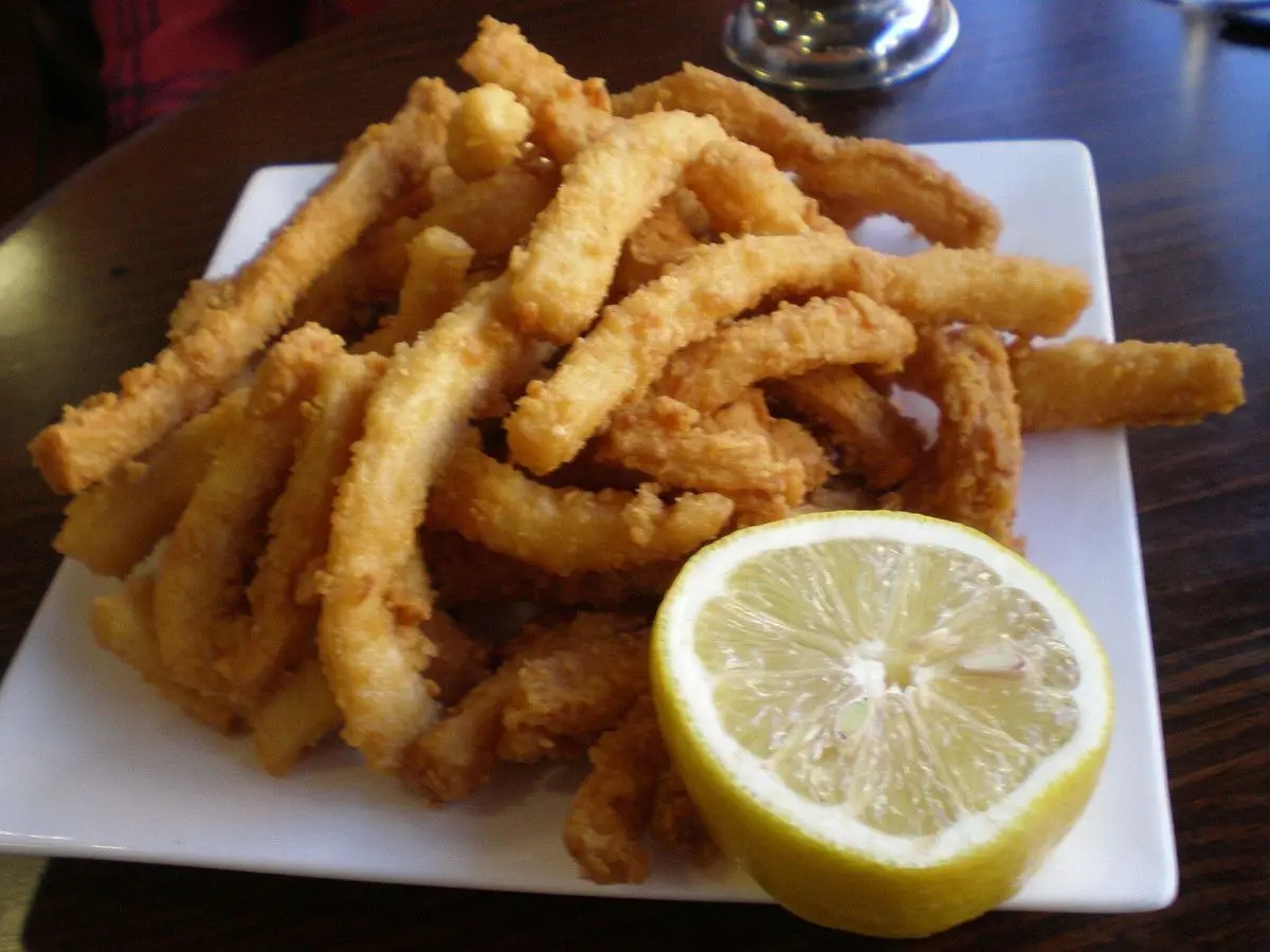 Plato de tiras de calamar rebozadas y fritas con medio limón sobre la mesa