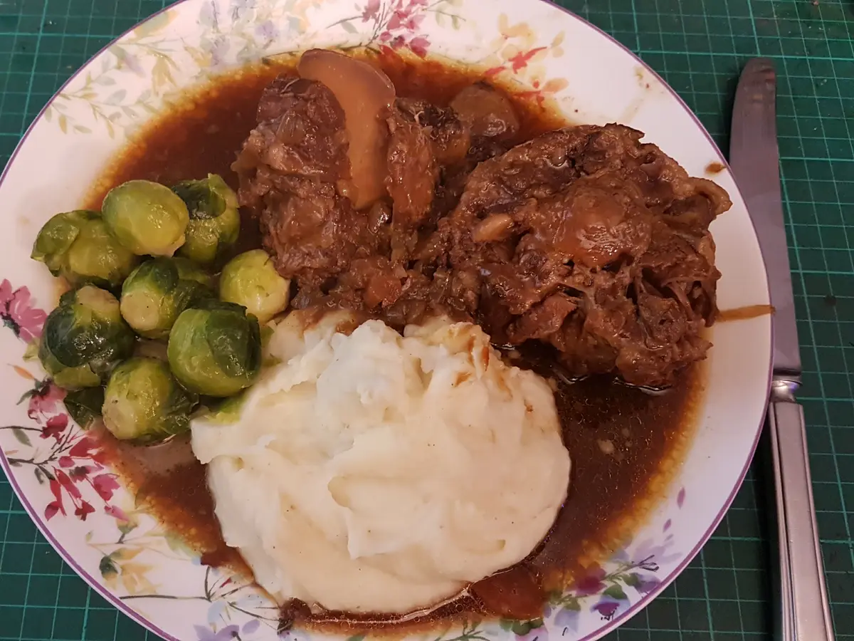 Rabo de buey estofado en salsa oscura con puré de patata y coles de Bruselas en un plato floreado
