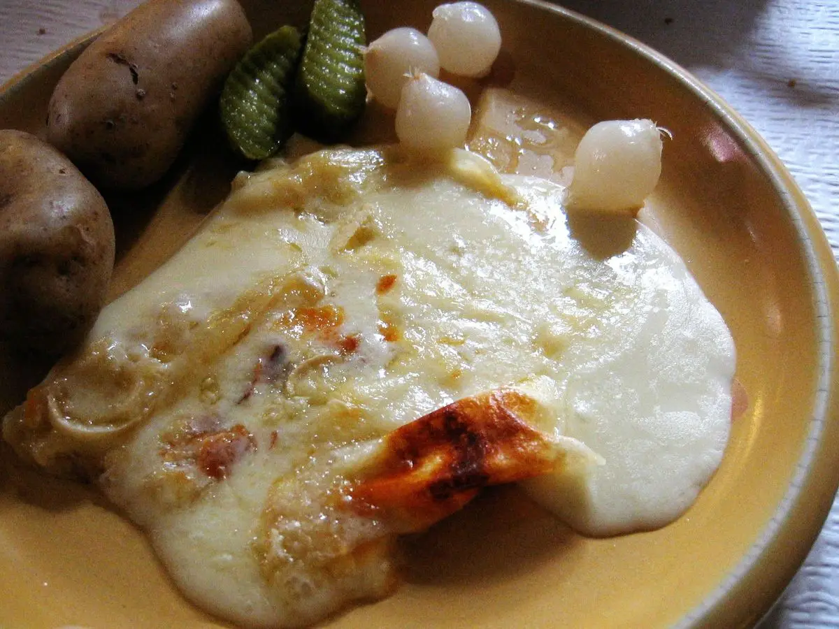 Raclette de queso fundido con patatas, pepinillos y cebollitas en un plato