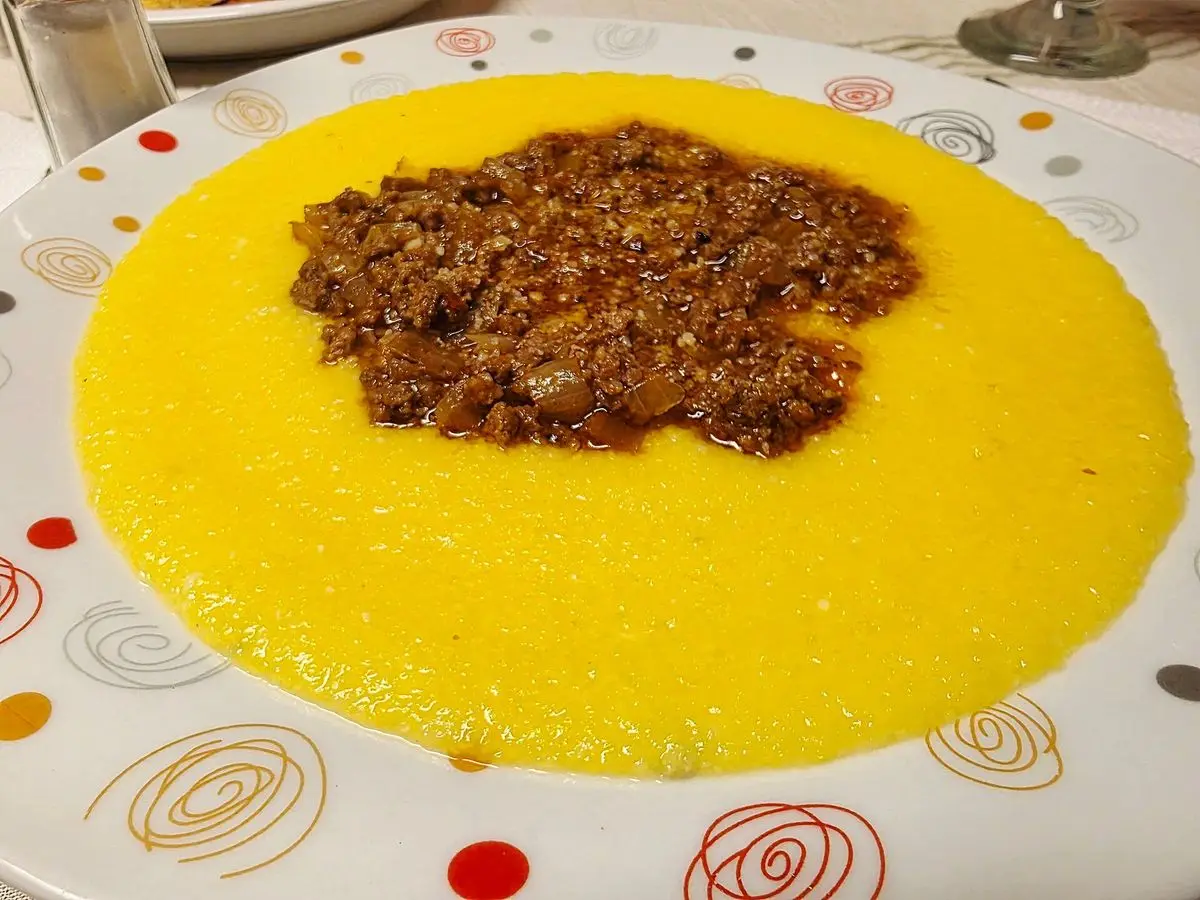 Plato de polenta cremosa amarilla con un ragú de carne picada en el centro