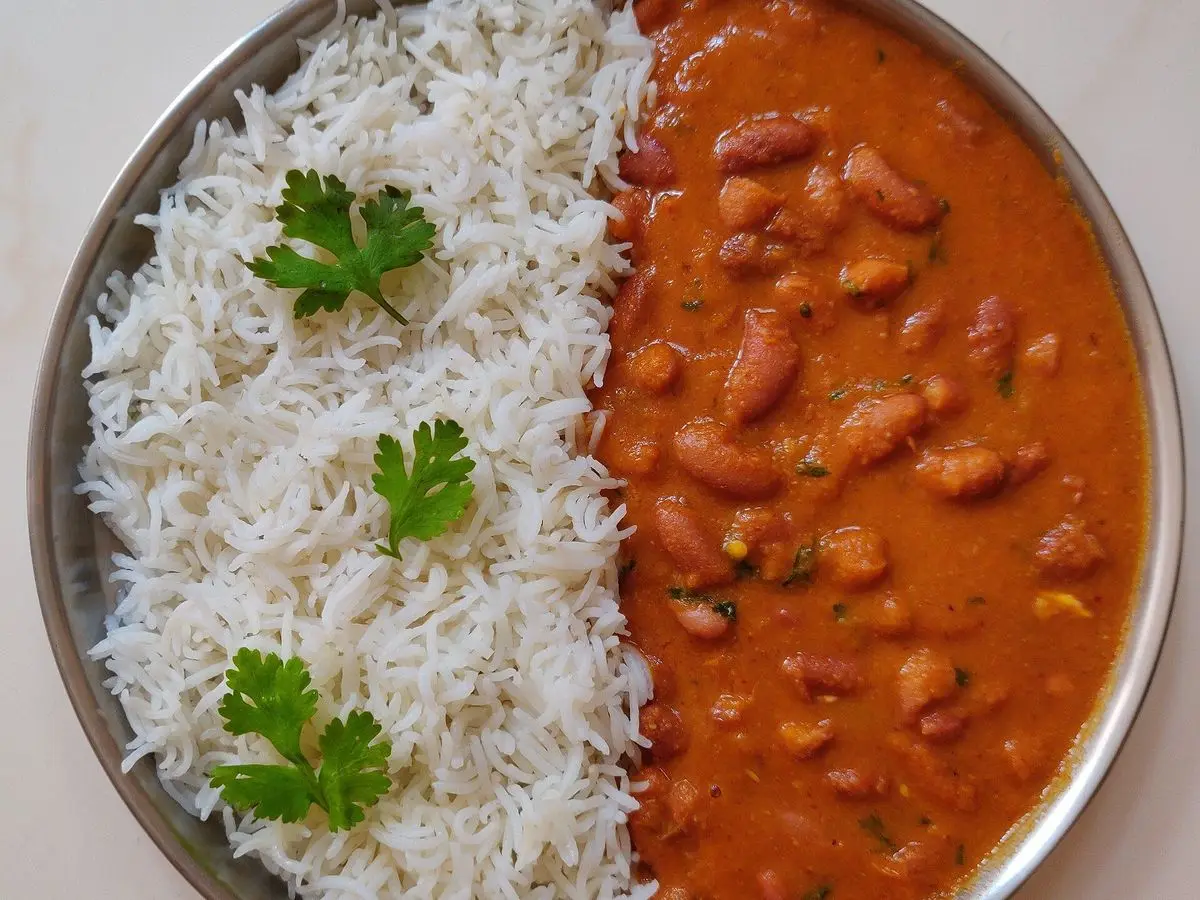 Plato metálico con arroz basmati blanco y curry de alubias rojas en salsa naranja, con hojas de cilantro