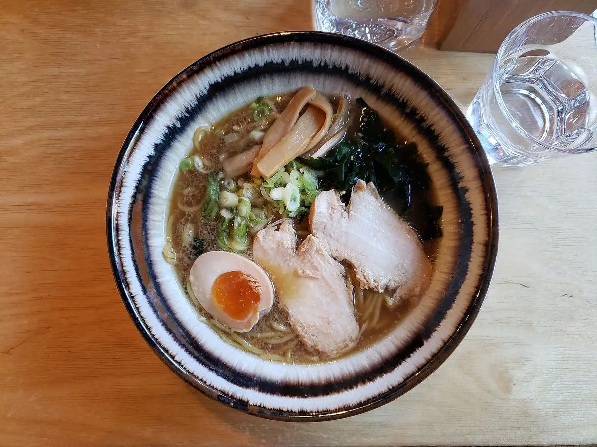 Cuenco de ramen con lonchas de pollo, huevo cocido partido, alga y cebolleta en caldo
