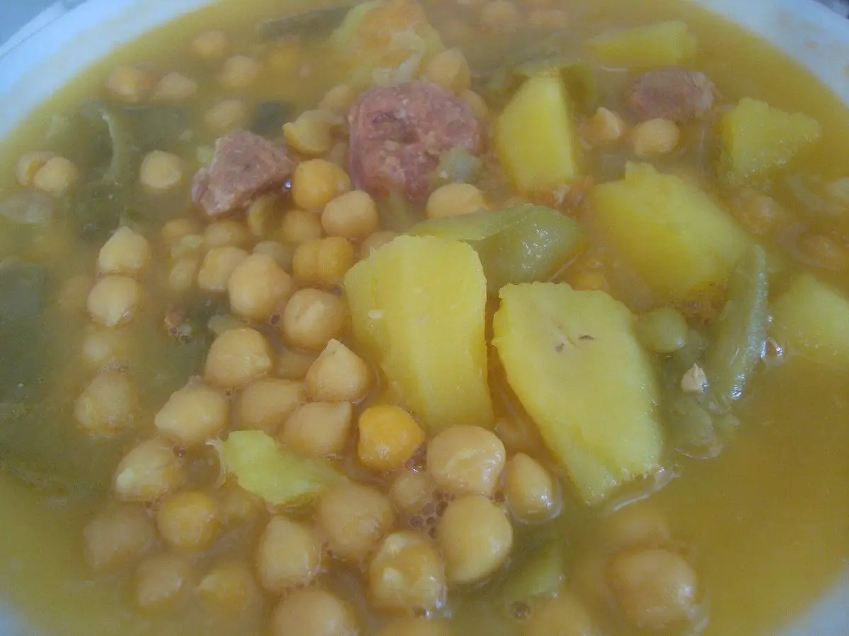 Plato de caldo con garbanzos, trozos de patata, carne y verdura en un caldo dorado