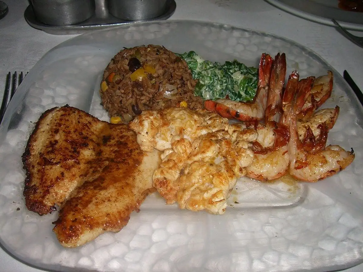 Pescado empanado con langostinos fritos, arroz y espinacas servidos en un plato de cristal