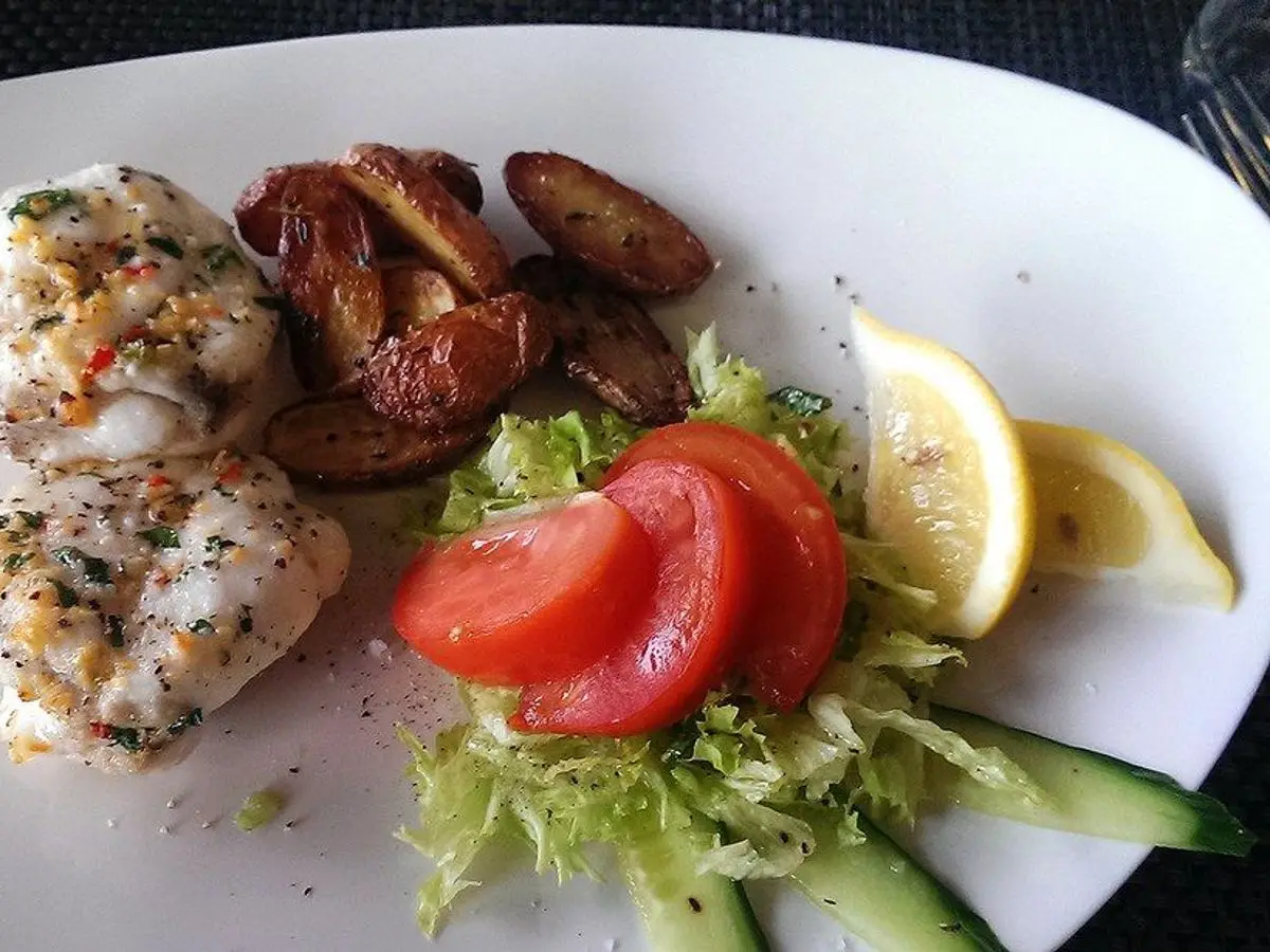 Filetes de pescado blanco con champiñones salteados, rodajas de tomate y lechuga en un plato