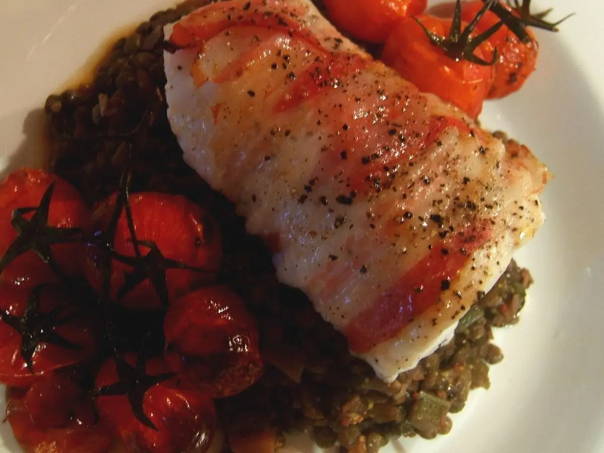 Lomo de pescado blanco envuelto en jamón curado sobre lentejas con tomates cherry asados