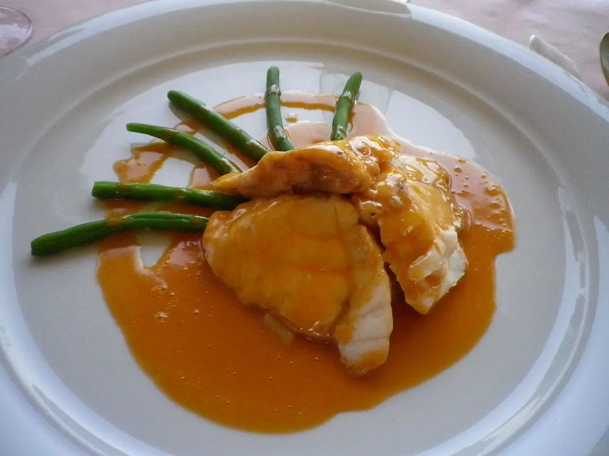 Medallones de rape con salsa naranja y judías verdes finas en un plato blanco